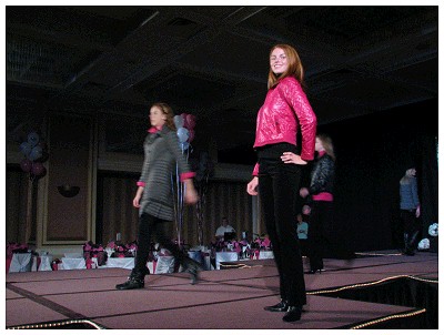 (Image: One Model Poses for the Camera while
 Another Walks in the Background)