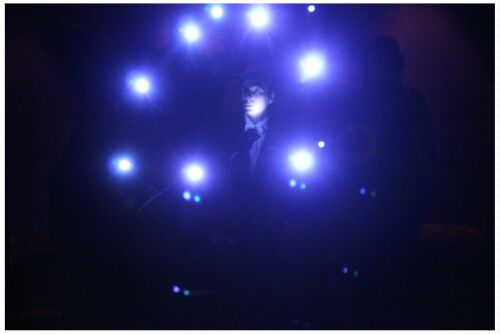 (Image: Dancers Surrounding the MC Point their Flashlights to
  the Audience)