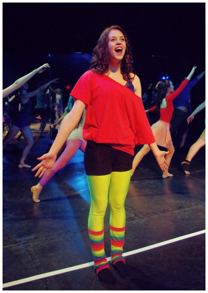 (Image: A Cast Member Sings while the Chorus Dances Behind)