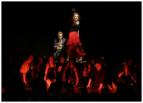 (Image: Two Principles on an Upstage Platform
        while the Chorus Kneels Facing Away from It)