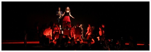 (Image: Two Principles on an Upstage Platform
        while the Chorus Dances All Around)