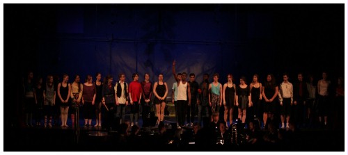 (Image: A Line of Dancers Stands Downstage 
        in Front of a Projected Pattern on the Rear Wall)