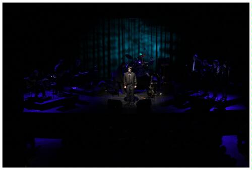 (Image: The Band is Bathed from Behind in Deep Blue
 while `Roy' Sings without Guitar)